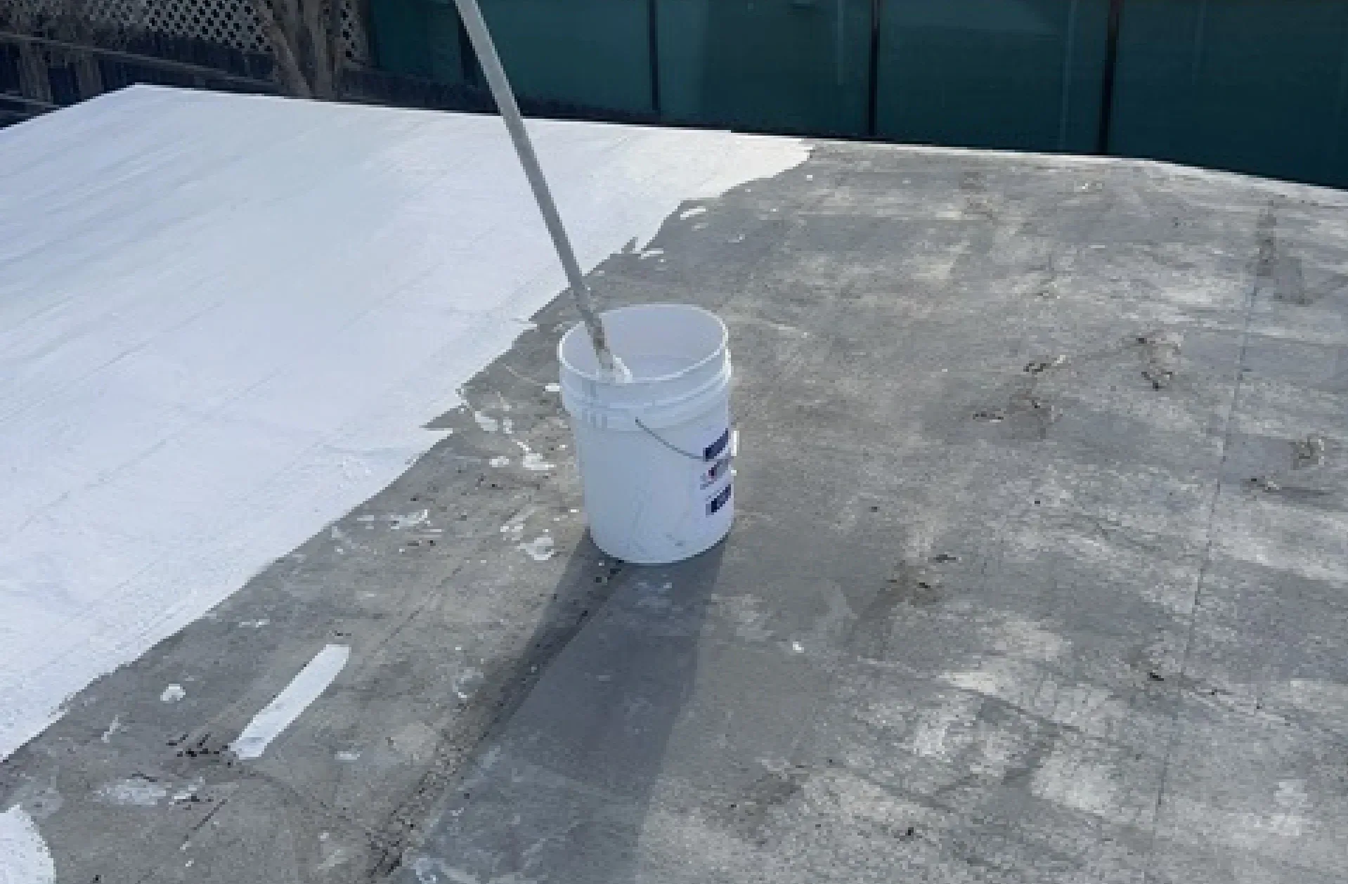 A flat roof half coated in white, with the roller and bucket beside it