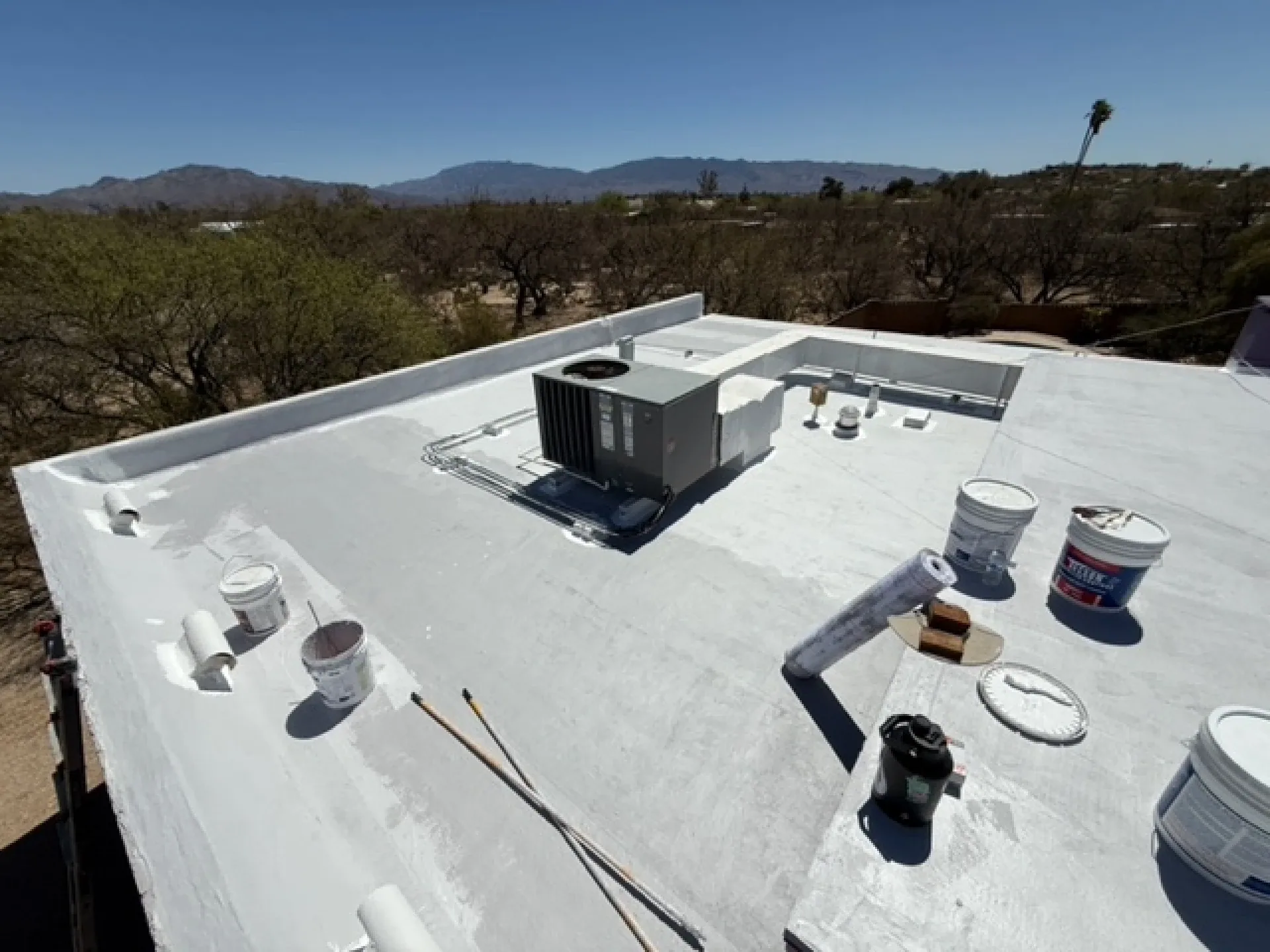 A crew member coating a flat roof with the Sonoran hills behind